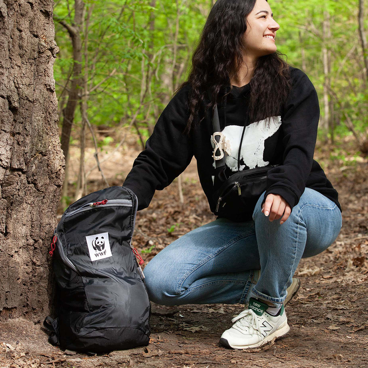A photo of a woman crouching next to the ChicoBag travel backpack featuring the WWF logo